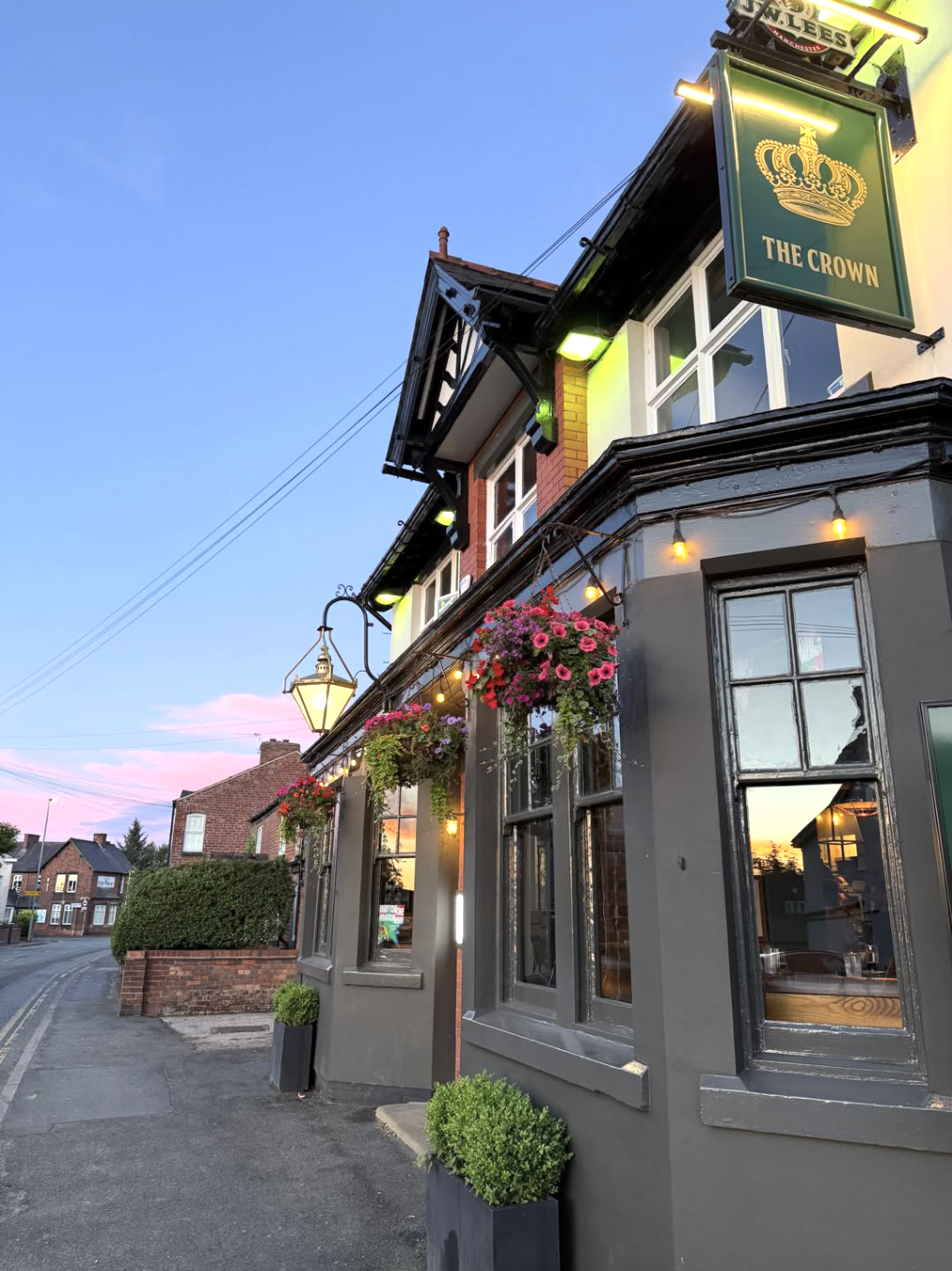 The Crown Lymm at dusk with hanging baskets and lit pub sign
